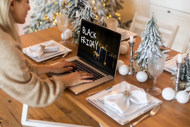 Mulher a fazer compras online para a Black Friday, numa mesa com decorações de Natal.