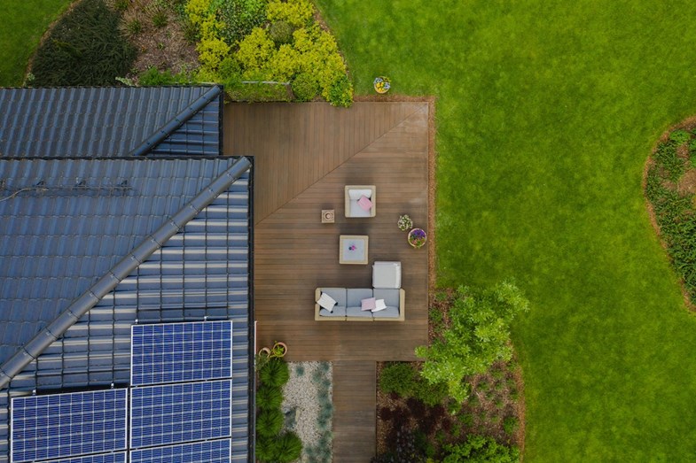 Vista aérea de moradia com painéis solares e terraço com um deck de madeira mobilado com decoração de jardim