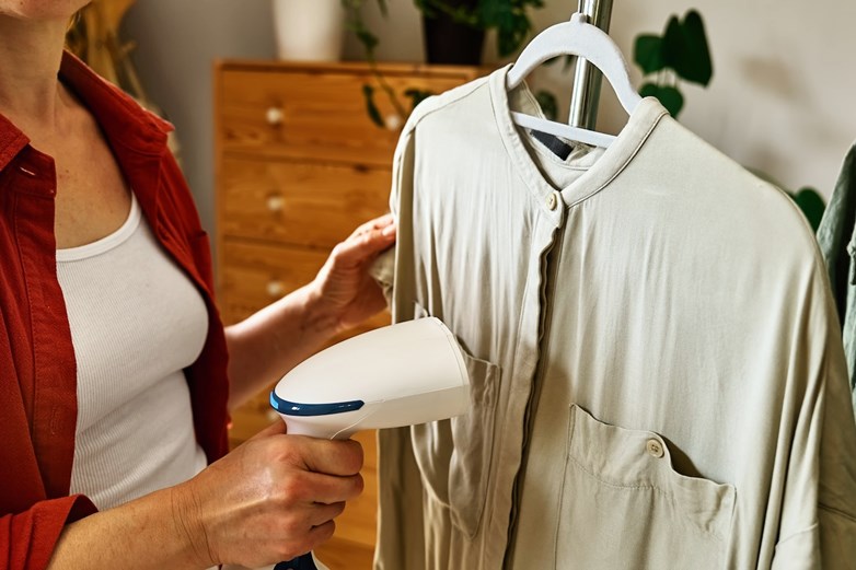 Mulher a utilizar um aparelho de engomar a vapor numa camisa branca pendurada num cabide