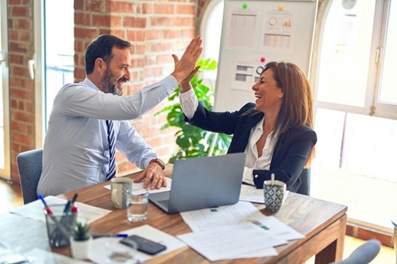 Dois profissionais de negócios celebram uma conquista com um "high five" numa secretária