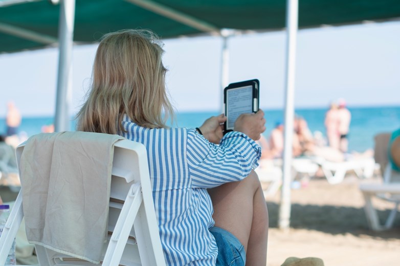 Mulher a ler um livro num e-reader na praia, debaixo de uma sombra