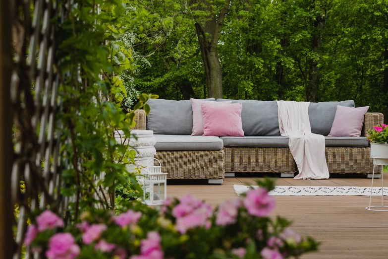 Terraço acolhedor com sofá de vime e almofadas cinzentas e rosa