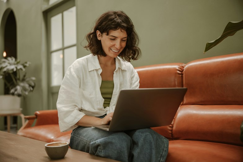 Mulher sentada num sofá vermelho com um computador ao colo.