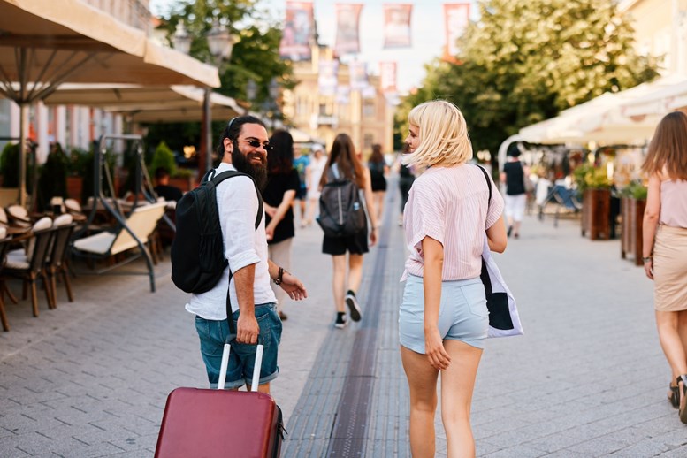 Um homem e uma mulher numa rua movimentada com lojas e cafés, a desfrutar de um passeio de verão ou de férias