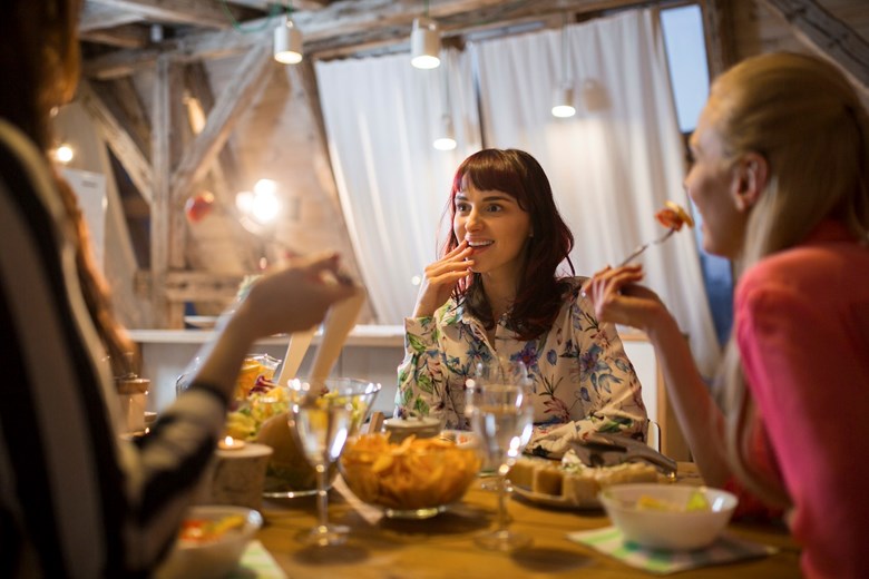 Três mulheres sentadas à mesa, a comer e a conversar durante uma refeição.