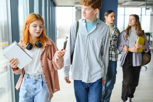 Grupo de estudantes do secundário a caminhar no corredor de uma escola, com uma rapariga a segurar um caderno em primeiro plano