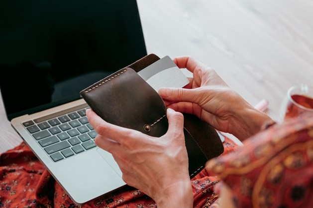 Pessoa coloca um cartão de crédito numa carteira de couro depois de fazer compras online