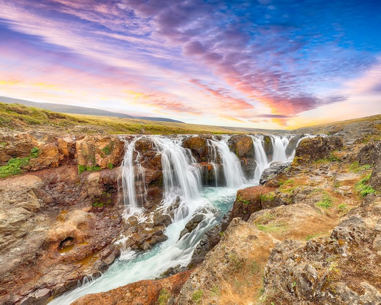 A cascata do desfiladeiro de Kolugljúfur, na Islândia, onde majestosas cascatas se derramam sobre penhascos rochosos sob um céu colorido ao pôr do sol