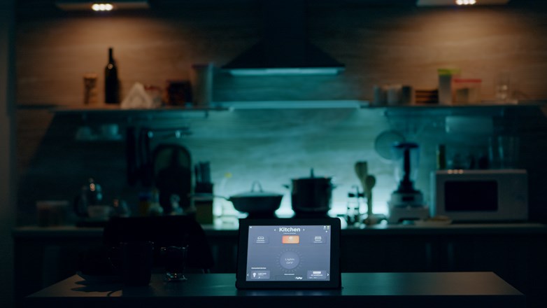 Smart kitchen escurecida, em que um tablet em grande plano exibe uma interface de controlo de vários eletrodomésticos através da rede de Wi-Fi.