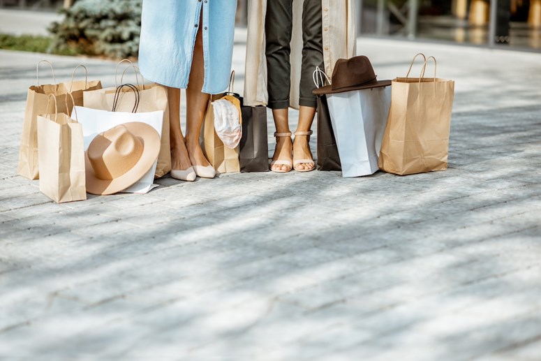 Duas mulheres num passeio com vários sacos de compras no chão aos seus pés